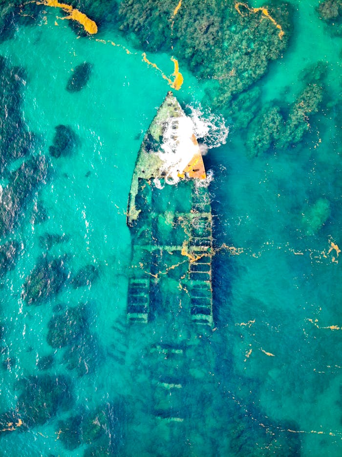 Drone captures stunning aerial shot of a sunken ship in crystal clear waters, revealing intricate details.